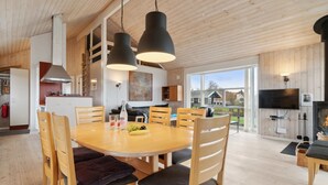 Une cuisine moderne avec des meubles en bois, un coin repas avec une table ronde et des chaises, et un salon avec un téléviseur et une cheminée.