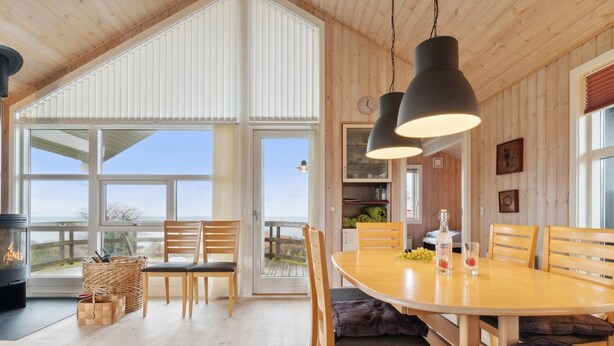 Un vaste espace dédié à la salle à manger, avec une grande table en bois, de nombreuses chaises et une vue sur l’extérieur grâce à de grandes fenêtres.