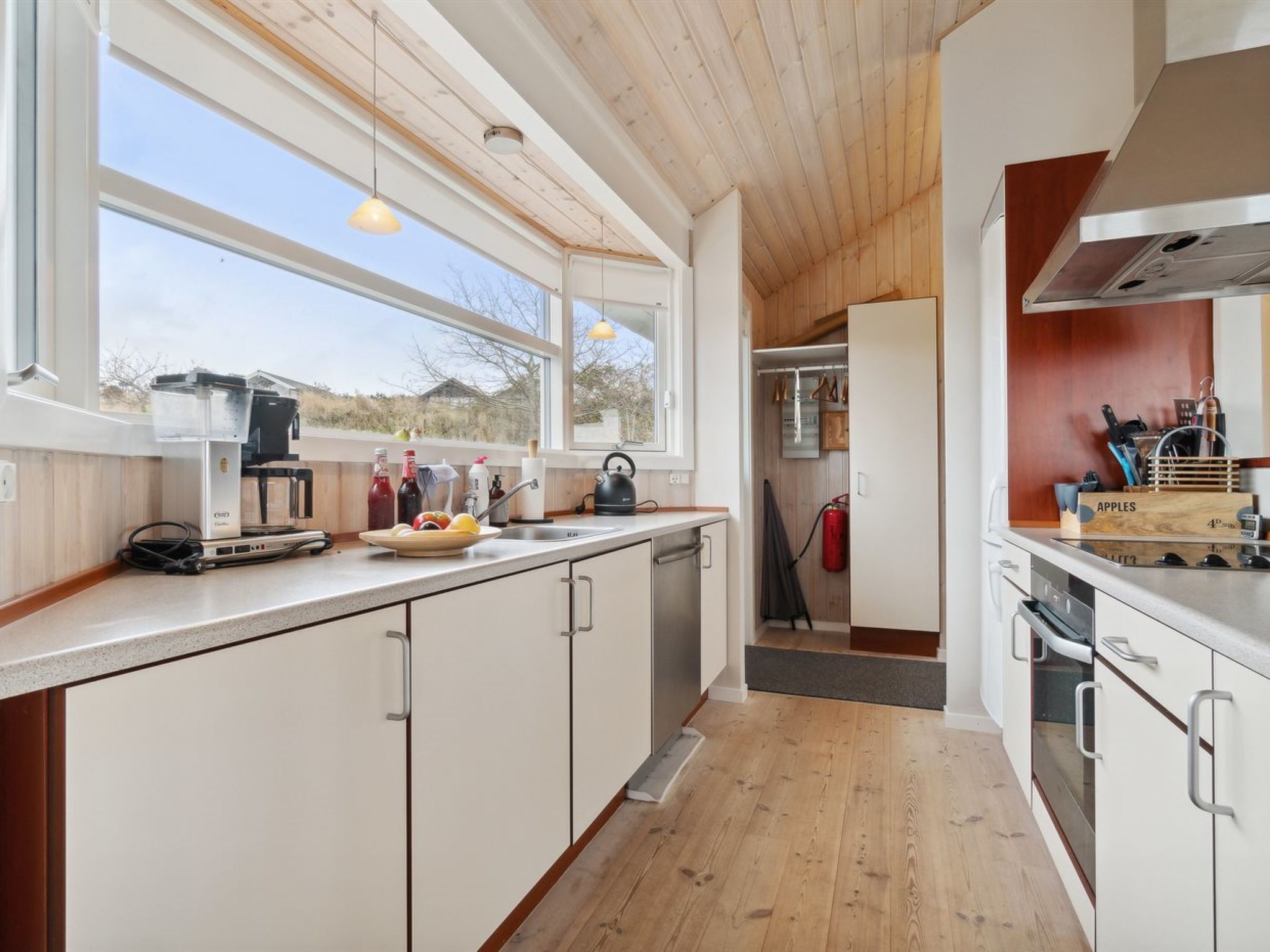 A modern kitchen with wooden cabinets, a built-in oven, and a large window providing natural light.