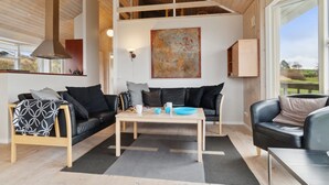 Un salon moderne avec un plafond haut, des poutres en bois, une grande peinture abstraite et une vue sur l’extérieur.