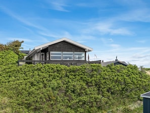 A modern house with a prominent overhang, surrounded by dense greenery.