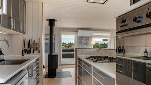 Cozinha moderna com eletrodomésticos de aço inoxidável, piso de madeira e vista pela porta.