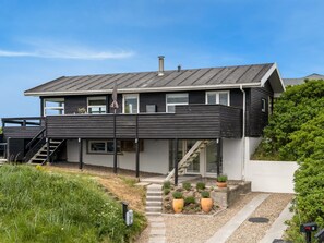 Une maison moderne à deux étages, dotée d’un toit plat, d’un balcon et d’un escalier menant à l’étage supérieur.
