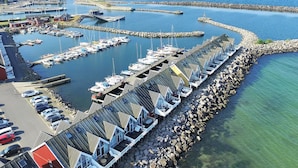 Una marina costanera amb diverses places d'amarra i embarcacions, una filera de cabanes de platja al llarg de la riba, i una vista clara del mar.