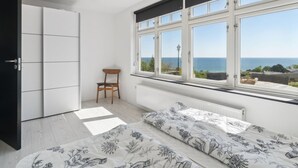 Un dormitorio con un ventanal grande, una cama con ropa de cama floral, una silla y un armario.