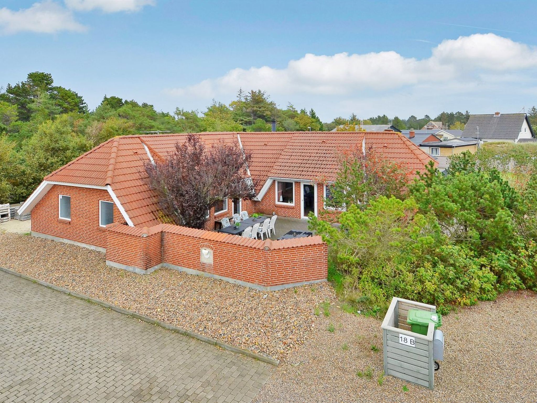 Ein Backsteinhaus mit geneigtem Dach, einer Terrasse und einer Schotterauffahrt.