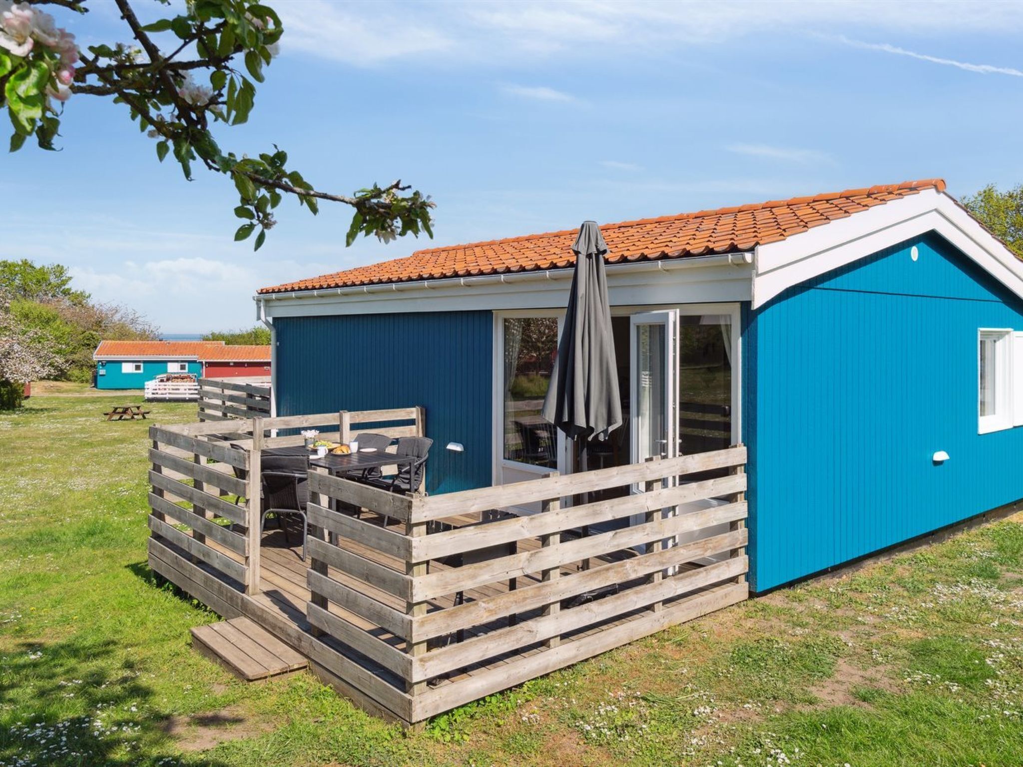 A small, single-story blue cabin with a tiled roof, a wooden deck, and a sliding glass door.
