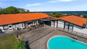 A poolside area with a wooden deck, a swimming pool, and a building with orange tiled roofs. - "Kjera" - 200m from the sea by Interhome (Allinge)