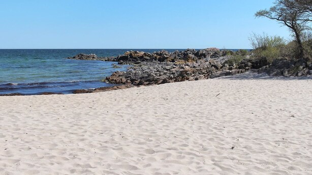 En sandstrand med klippformationer och gles växtlighet.