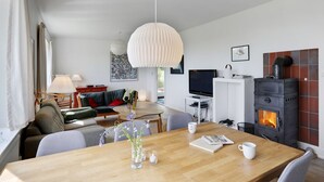Ett modernt vardagsrum med ett matbord i trä, en soffa, en tv och en öppen spis.