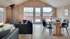 Un interno moderno di una baita, con arredamento in legno, un'area pranzo e un'ampia finestra vista un recinto rosso.