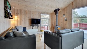 Un soggiorno moderno con rivestimenti in legno, un divano in pelle nera, un tavolino da caffè bianco e un televisore.