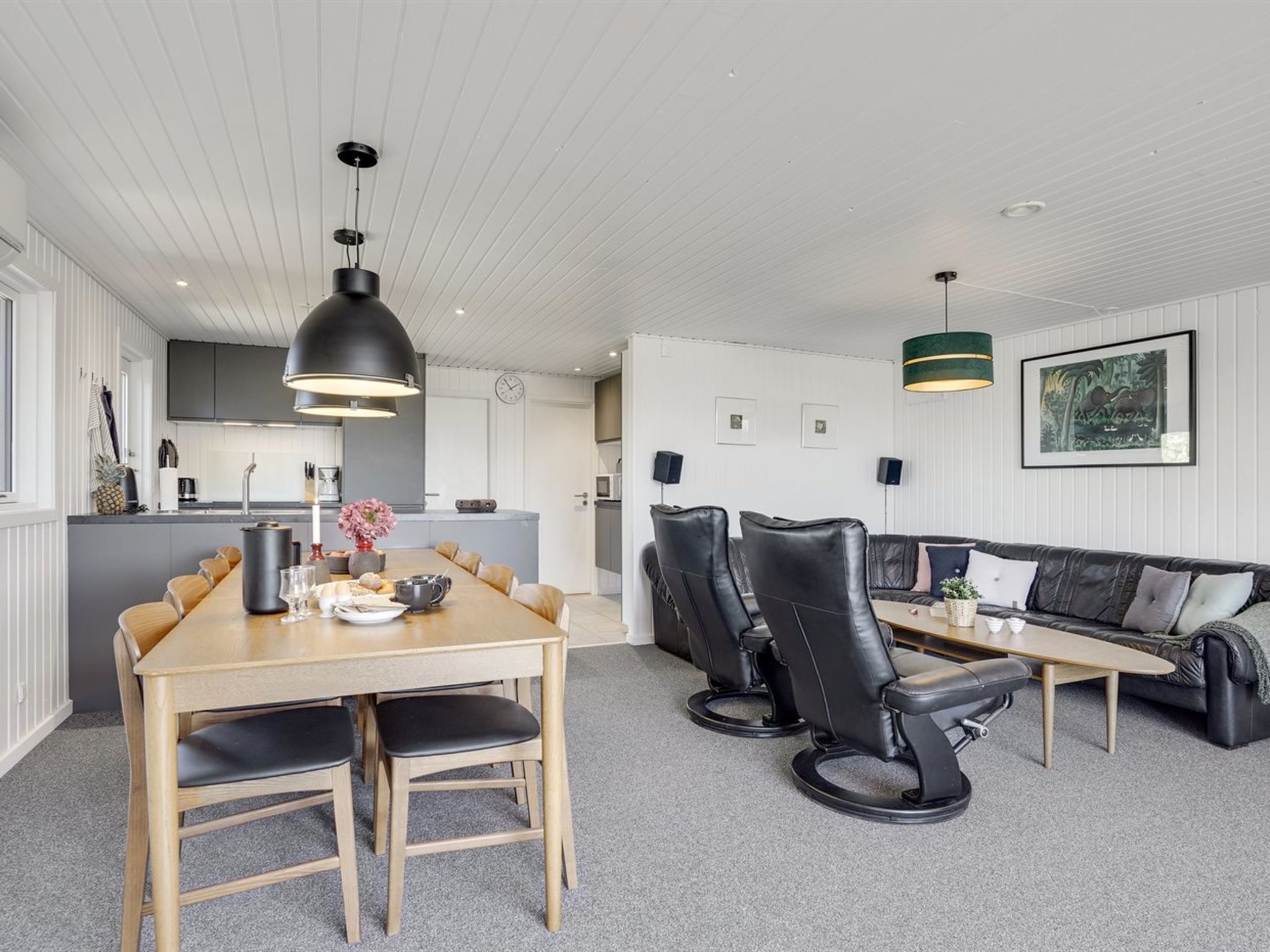 Une cuisine moderne avec des meubles blancs, un coin repas avec une table et des chaises en bois, et un salon avec un canapé et une table basse.