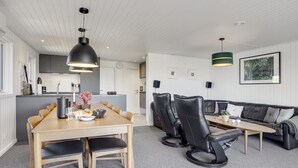 Une cuisine moderne avec des meubles blancs, un coin repas avec une table et des chaises en bois, et un salon avec un canapé et une table basse.