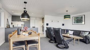Une cuisine moderne avec des meubles blancs, un coin repas avec une table et des chaises en bois, et un salon avec un canapé et une table basse.