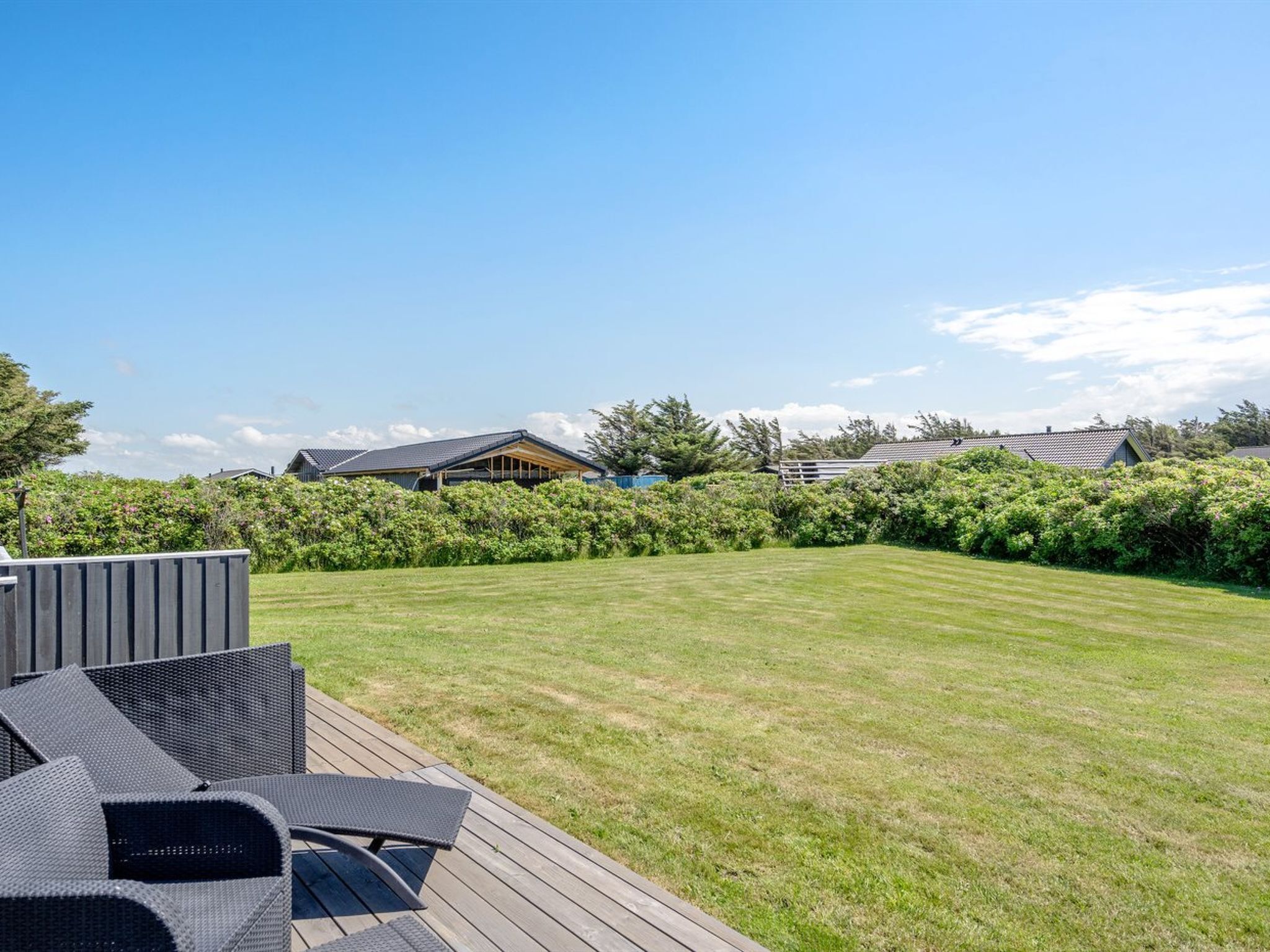 Un jardin bien entretenu, avec une terrasse en bois, du mobilier d’extérieur et une pelouse soigneusement taillée.