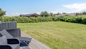 Un jardin bien entretenu, avec une terrasse en bois, du mobilier d’extérieur et une pelouse soigneusement taillée.