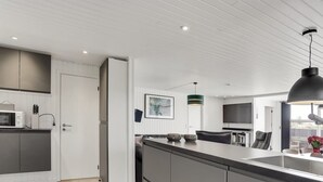 Une cuisine moderne dotée d’un grand îlot central, de meubles blancs et d’un coin repas avec une chaise et une table noires.