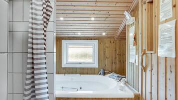 Une salle de bain moderne avec un intérieur en bois, une grande baignoire, une fenêtre et divers équipements.