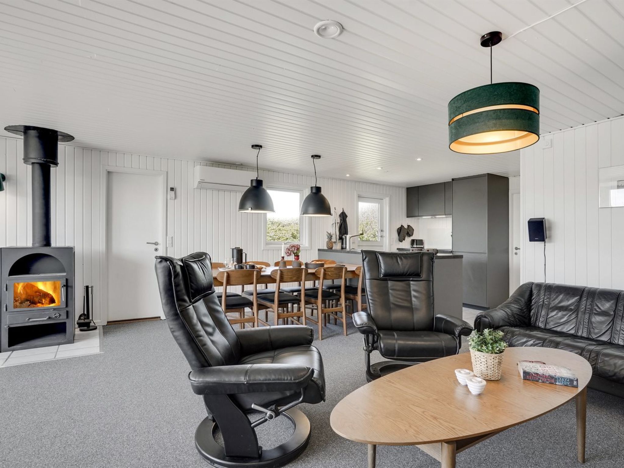 En moderne stue med pejs, læderstole, et træsofabord og hængende lamper.