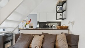 A modern bedroom with a loft-style ceiling, a bed with grey bedding, a small kitchenette, and a decorative wall shelf.