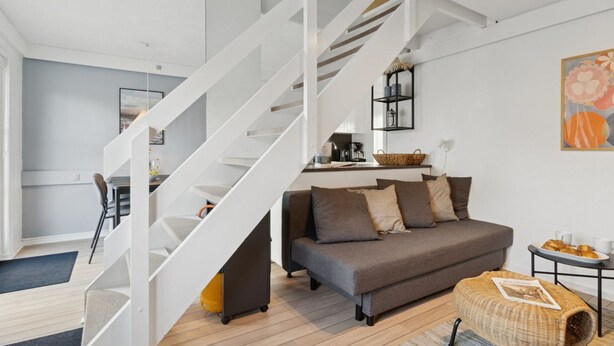 A modern living room with a staircase, a sofa, a coffee table, and a basket.
