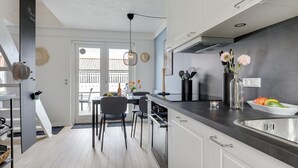 A modern kitchen with white cabinets, a black countertop, and a dining area with chairs and a table.
