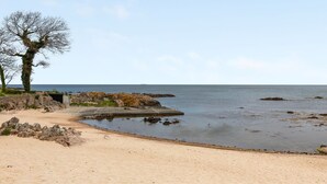 A coastal beach with a sandy shore, rocky outcrops, and a clear sky.