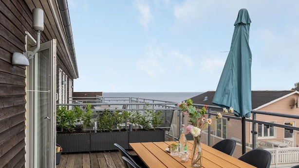 A wooden deck with a table and chairs, a covered umbrella, and potted plants.