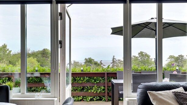 En uteplats med ett trädäck, en möblerad sittplats under tak med bord och stolar samt utsikt över havet.