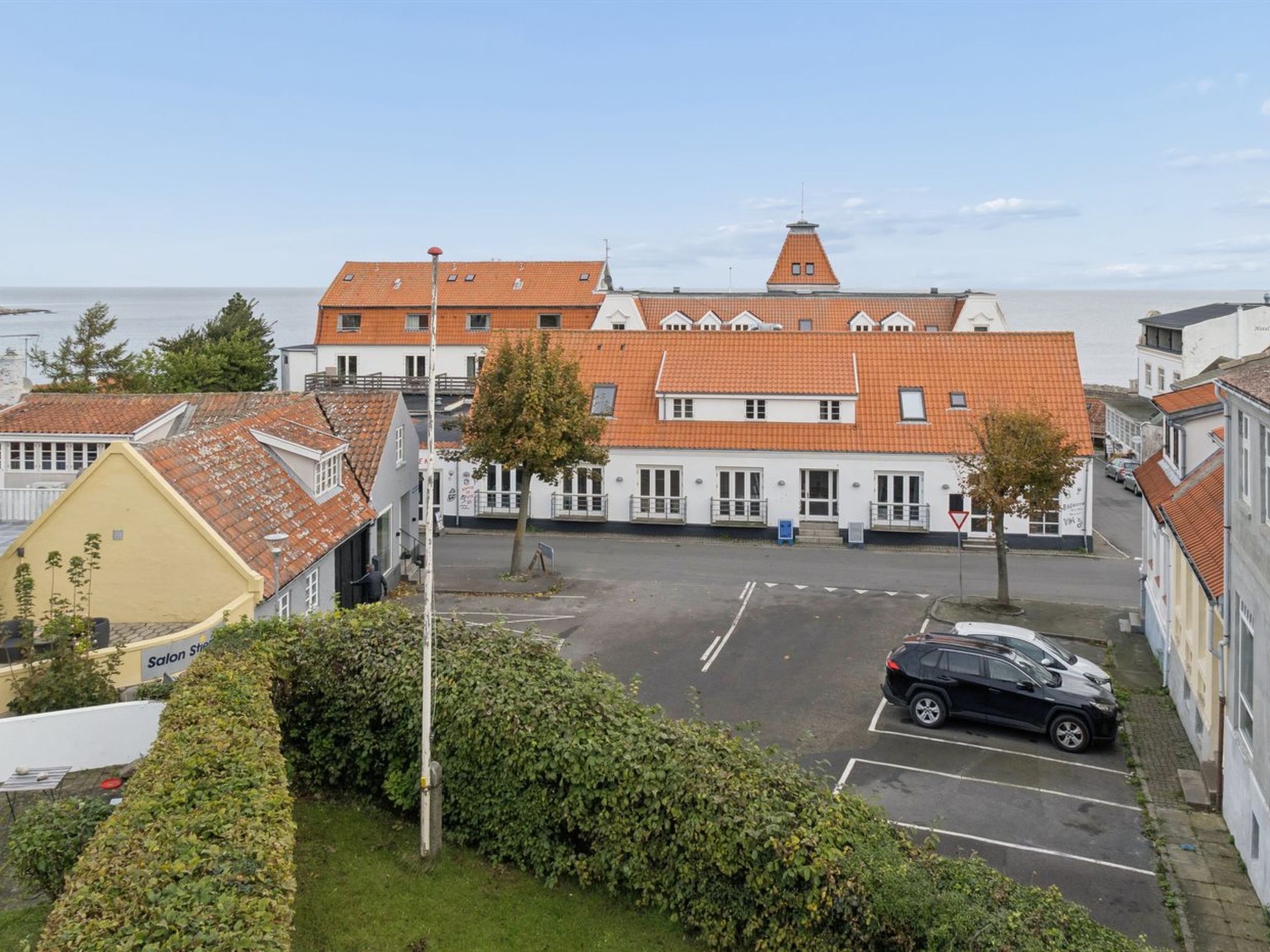 Ett hotell vid kusten med ett rött tegeltak, en parkeringsplats och utsikt över havet.