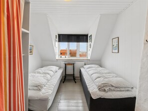 A dormitory room with two single beds, a small table, and a window with blinds.