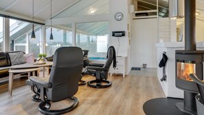 Ein modernes Wohnzimmer mit Kamin, Ledersesseln, einem Esstisch und großen Fenstern.