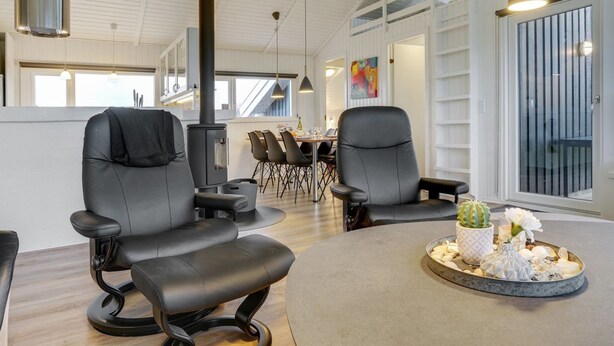 Ein modernes Interieur mit zwei schwarzen Ledersesseln, einem Esstisch mit Stühlen, einem großen Fenster und einem dekorativen Kaktus als Mittelstück.