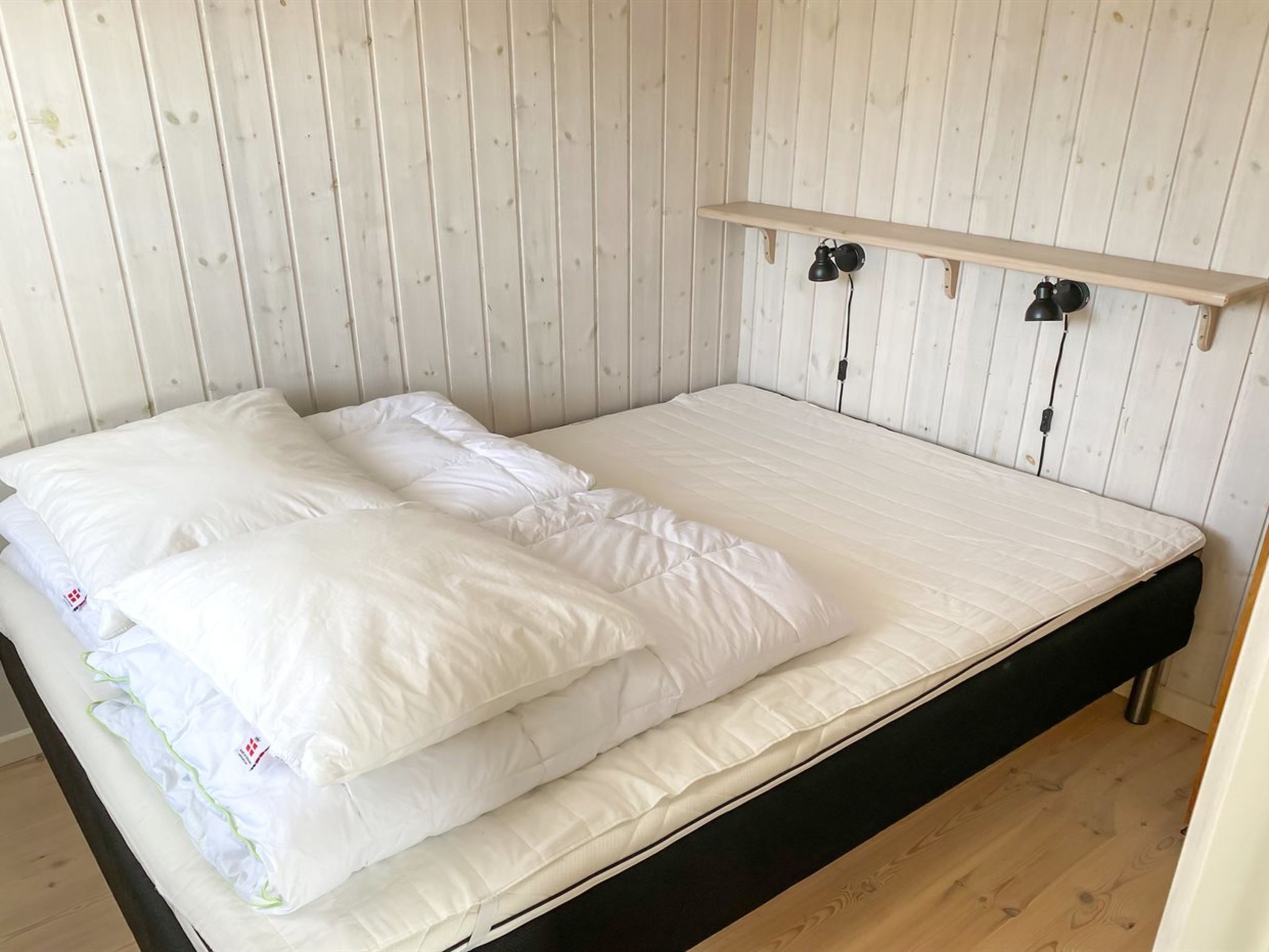 A single-bed room with a wooden headboard, a shelf above the bed, and a black metal stand.