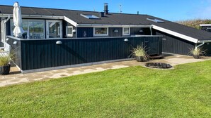 Une maison moderne à l’extérieur bleu foncé, dotée d’un patio couvert et d’une pelouse bien entretenue.