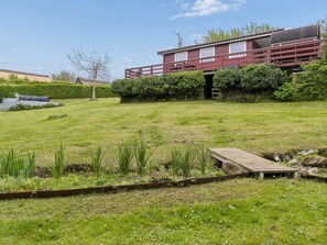 Una propiedad residencial con césped cuidado, una terraza de madera y un edificio rojo con balcón.