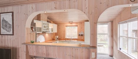 Puisesti sisustettu tila, jossa on keittiö, kaksi baarijakkaraa ja suuri ikkuna.