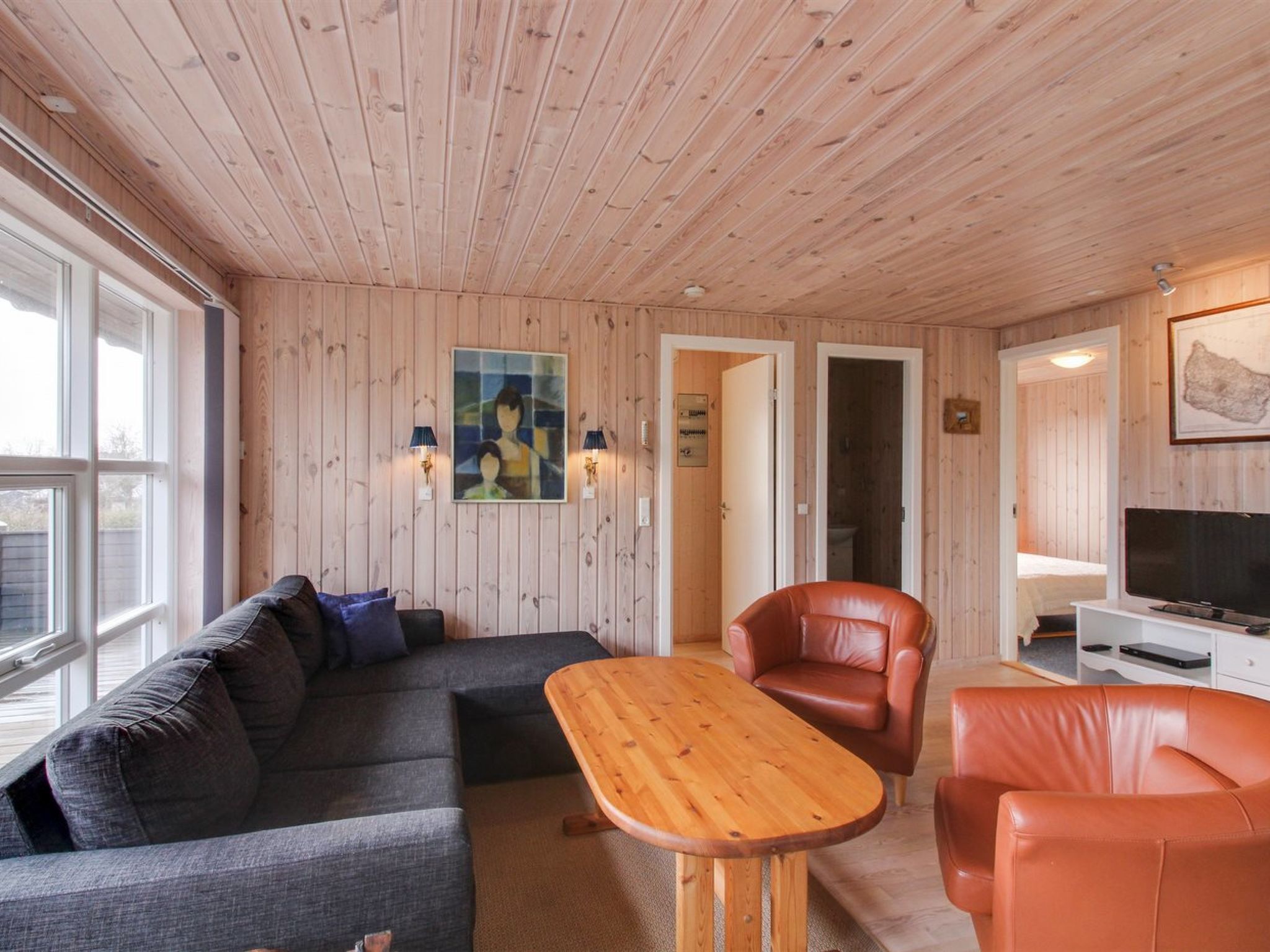 A cozy room with a wooden ceiling, a sofa, a leather chair, a wooden table, and a TV.