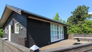Eine Holzhütte mit einer Veranda, großen Fenstern und blauem Himmel.