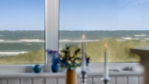 Een kamer met uitzicht op de oceaan door een groot raam, een wastafel en een vaas met bloemen.