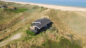Een modern huis met een plat dak, gelegen op een duin met uitzicht op strand en zee.
