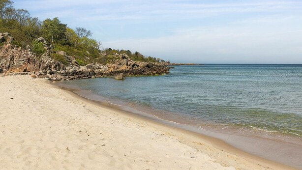 Une plage de sable avec des affleurements rocheux et une eau calme.