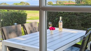 Une table avec une bouteille de vin, un verre et une rose, le tout placé devant un paysage verdoyant et la mer.