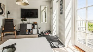 Une chambre moderne avec un grand lit, une télévision, un fauteuil, une bibliothèque et une fenêtre donnant sur un beau paysage.