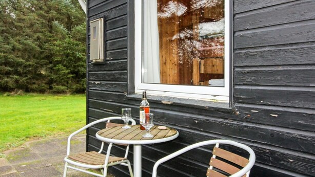A wooden exterior with a window, a small table with two chairs, and a bottle of drink.