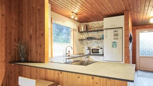 A compact kitchen with wooden walls, a central island, two bar stools, a microwave, and a refrigerator.