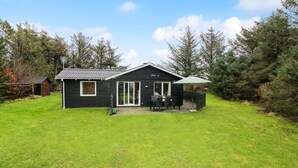 A black cabin with a patio, a small shed, and a grassy yard.