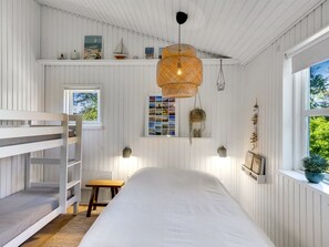 Ein Zimmer mit einem Etagenbett, einem kleinen Tisch, einer Deckenleuchte, einem Fenster mit Blick und an Wänden befestigten Regalen mit Dekoration.
