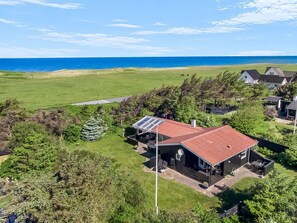 Une propriété située sur la côte, avec une maison dotée d’un toit rouge, de panneaux solaires et d’une terrasse aménagée avec du mobilier d’extérieur.